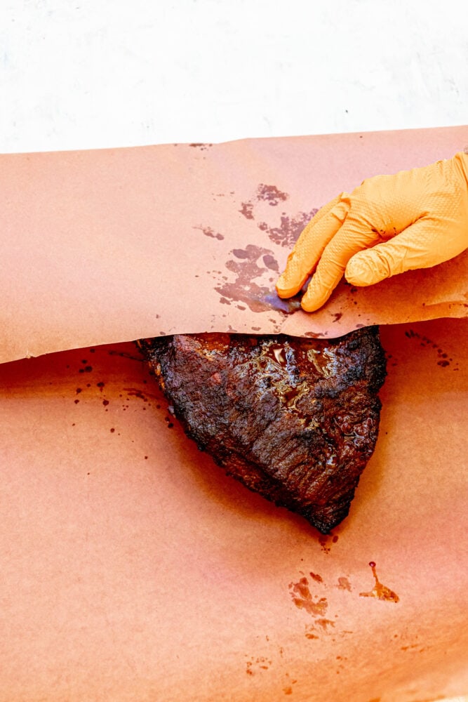 a hand wrapping brisket in paper